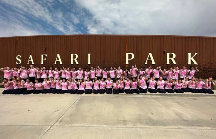 Australian Girls Choir stand in pink tshirts in from of Safari Park sign