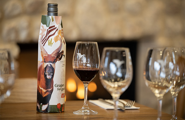 Glasses of red wine on a wooden table with a bottle of wine in sleeve with Bongo image