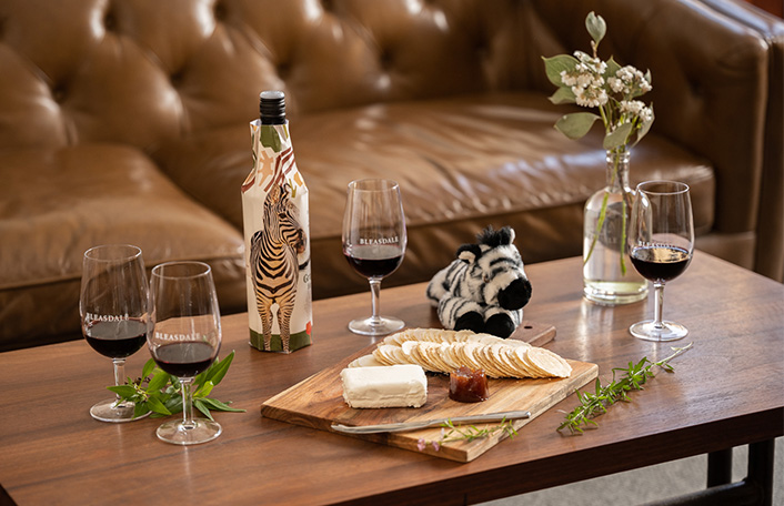 Bottle of Grapes for Good wine rests on timber table with wine glasses and a cheese board