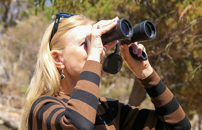 Woman with long blonde hair holding binoculars up to her face to look through them